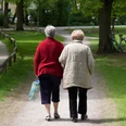 Aeltere Damen beim Spaziergang_c_AdobeStock_13657830_FelixSchollmeyer_ .jpeg Zwei ältere Damen spazieren Arm in Arm auf einem schattigen Parkweg, umgeben von grünen Bäumen.