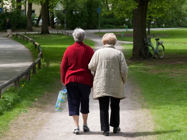 Aeltere Damen beim Spaziergang_c_AdobeStock_13657830_FelixSchollmeyer_ .jpeg Zwei ältere Damen spazieren Arm in Arm auf einem schattigen Parkweg, umgeben von grünen Bäumen.