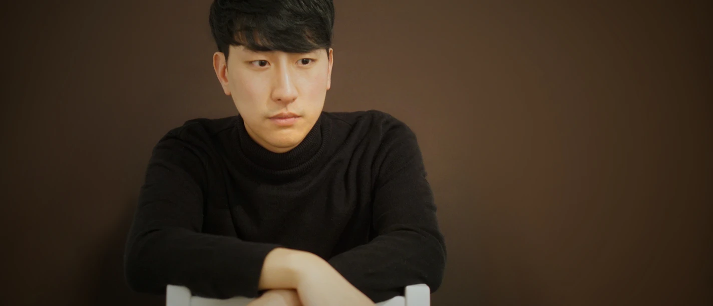 Weltklassik am Klavier: Henley Jun Een persoon in een zwarte coltrui zit nadenkend op een stoel met zijn armen over elkaar.