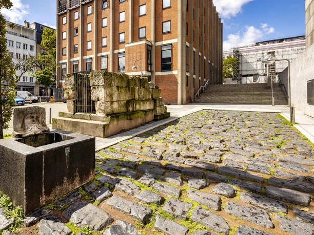 Römische Hafenstraße Römische Hafenstraße in Köln mit altem Mauerwerk, gepflastertem Weg und modernem Gebäude im Hintergrund.