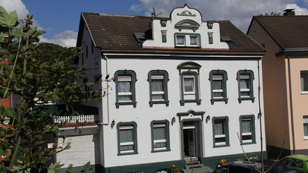 Historische weiße Villa mit grünen Details, befindet sich in einer ruhigen Wohngegend bei Sonnenschein.