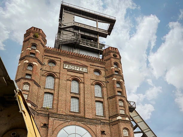Malakoffturm, Bottrop ```html <p>Alte Zeche Prosper, roter Backsteinbau mit hohen Fenstern und Förderturm, im Vordergrund ein Zug.</p> ```