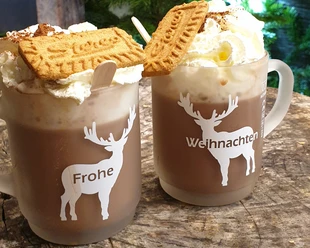 Zwei Tassen Kakao mit aufwändigem Sahnehäubchen, verziert mit Spekulatius, auf einer Holztischplatte.