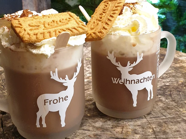 Weihnachtsmarkt Zwei Tassen Kakao mit aufwändigem Sahnehäubchen, verziert mit Spekulatius, auf einer Holztischplatte.
