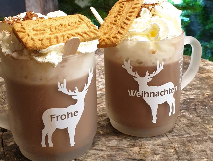 Weihnachtsmarkt Zwei Tassen Kakao mit aufwändigem Sahnehäubchen, verziert mit Spekulatius, auf einer Holztischplatte.