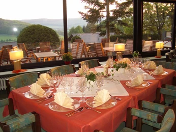 Hotel Waldcafe Jäger Bad Driburg_Restaurant_Avenarius Wohlfühlhotels.jpg Restaurant mit stilvoll gedeckten Tischen innen; draußen hügelige Landschaft und Terrasse.