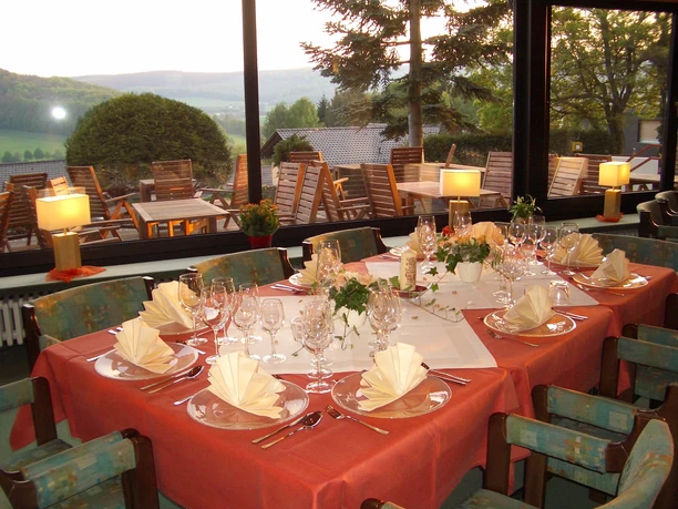 Hotel Waldcafe Jäger Bad Driburg_Restaurant_Avenarius Wohlfühlhotels.jpg Restaurant mit stilvoll gedeckten Tischen innen; draußen hügelige Landschaft und Terrasse.