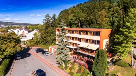 Hotel Waldcafe Jäger Bad Driburg_Komplettaufnahme_Avenarius Wohlfühlhotels_2500.jpg Hotel Waldcafe Jäger Bad Driburg umgeben von Bäumen mit Terrasse und angrenzendem Parkplatz