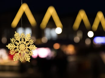 Weihnachtsmarkt Steinhagen Beleuchtung Ein leuchtender Schneekristall hängt vor unscharfem, festlich beleuchtetem Hintergrund bei Nacht.