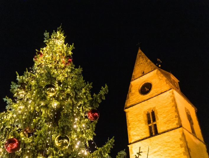Weihnachtsmarkt Steinhagen Kirche Beleuchteter Weihnachtsbaum neben einer beleuchteten Kirchturmspitze in festlicher Nachtatmosphäre.