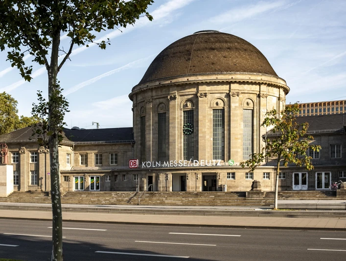Bahnhof KoelnMesse Deutz Historischer Empfangsbereich des Bahnhofs Köln Messe/Deutz mit markantem Kuppeldach unter blauem Himmel.Historic reception area of Cologne Messe/Deutz station with striking domed roof under a blue sky.