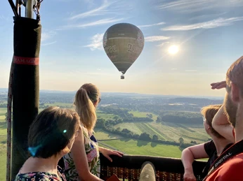 Blick-auf-den-Barre-Ballon.jpg Eine Gruppe von Menschen blickt aus einem Heißluftballon über eine weitläufige grüne Landschaft.