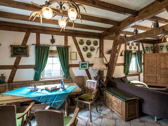 Ennenbach_Essen.jpg Gemütliches, rustikales Wohnzimmer mit Holzbalken, Esstisch, antiken Möbeln und Jagdtrophäen an der Wand.