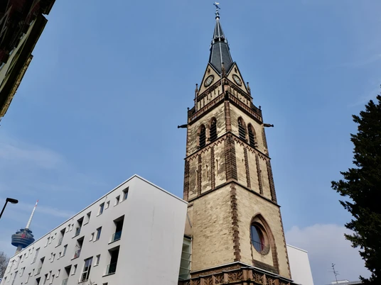 Christuskirche Turm der Christuskirche in Köln bei klarem Himmel, links modernere Gebäude, im Hintergrund ein Sendeturm.Tower of the Christuskirche in Cologne with clear skies, modern buildings on the left, and a transmission tower in the background.