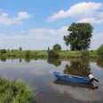 Weser bei Petershagen Windheim Ein ruhiger Flusslauf mit einem blauen Ruderboot im Vordergrund, umgeben von üppigem Grün und einem klaren Himmel mit weißen Wolken.