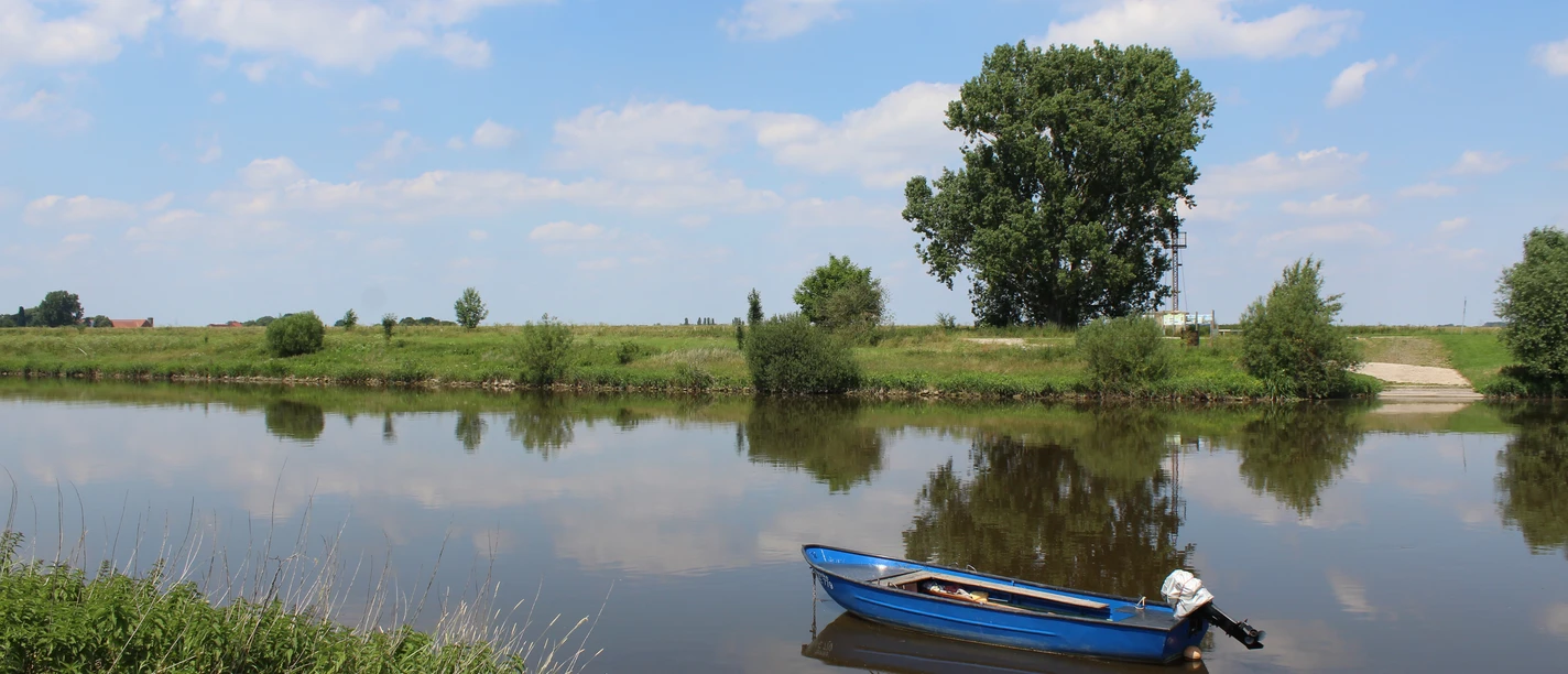 Weser bei Petershagen Windheim Ein ruhiger Flusslauf mit einem blauen Ruderboot im Vordergrund, umgeben von üppigem Grün und einem klaren Himmel mit weißen Wolken.