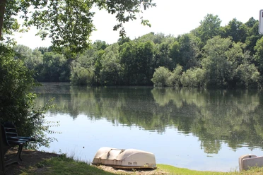 Campingplatz am Landwehrsee Ein ruhiger See mit umgebenden Bäumen und zwei kleinen Booten im Vordergrund bietet eine friedliche Naturkulisse.