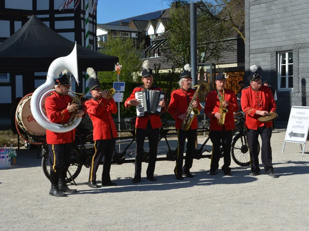 Eine Blaskapelle in roten Uniformen musiziert vor traditionellen Gebäuden bei strahlendem Sonnenschein.