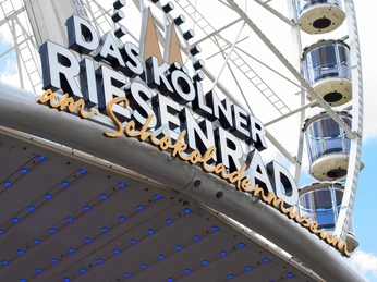 Kölner Riesenrad Kölner Riesenrad, verziert mit dem Schriftzug „Das Kölner Riesenrad am Schokoladenmuseum“ und strahlenden blauen Lichtern.Cologne Ferris wheel, decorated with the lettering "Das Kölner Riesenrad am Schokoladenmuseum" and bright blue lights.