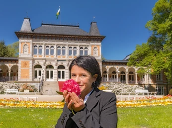 Rhododendronblüte©JanBräuer.jpg Eine Frau hält eine Rhododendronblüte vor einem historischen Gebäude.