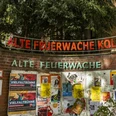 Alte Feuerwache Die Alte Feuerwache Köln mit einer Ziegelmauer voller bunter Plakate und einem leuchtenden Schriftzug oben.