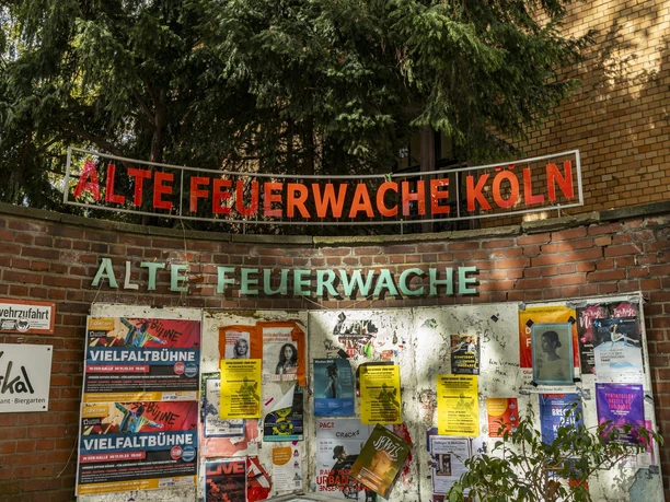 Alte Feuerwache Die Alte Feuerwache Köln mit einer Ziegelmauer voller bunter Plakate und einem leuchtenden Schriftzug oben.