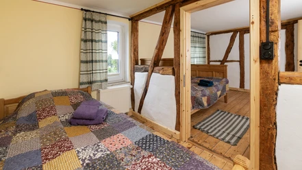 Zwei rustikale Schlafzimmer mit Holzbalken, Patchwork-Bettdecken und einem Fenster, das Licht hereinlässt.