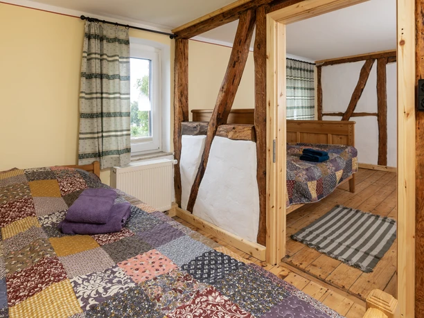 Zwei rustikale Schlafzimmer mit Holzbalken, Patchwork-Bettdecken und einem Fenster, das Licht hereinlässt.