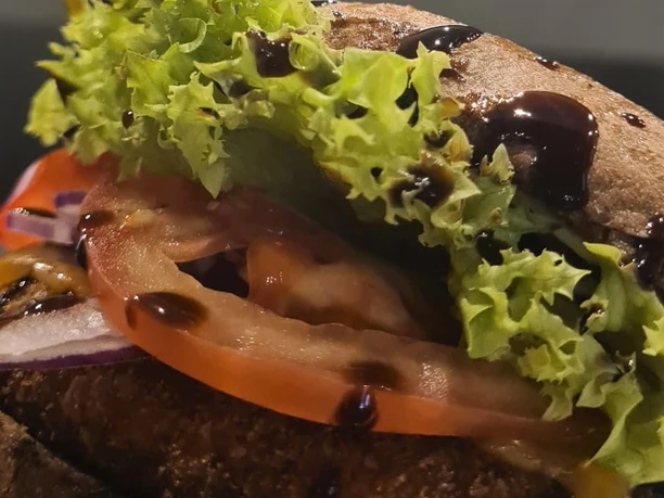 Ein saftiger Burger mit frischem Salat, Tomatenscheiben, roten Zwiebeln und krossem Brötchen.