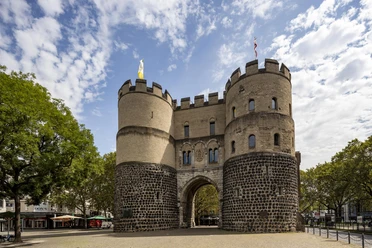 Hahnentorburg The picture shows the historic Hahnentor in Cologne, a massive stone fortress with two round towers under a blue sky.