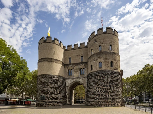 Hahnentorburg Das Bild zeigt das historische Hahnentor in Köln, eine massive Steinfestung mit zwei Rundtürmen unter blauem Himmel.The picture shows the historic Hahnentor in Cologne, a massive stone fortress with two round towers under a blue sky.