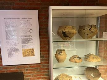 Vitrine mit Ausgrabungen Vitrine mit antiken Keramikgefäßen, die teilweise rekonstruiert sind, in einem Ausstellungsraum.