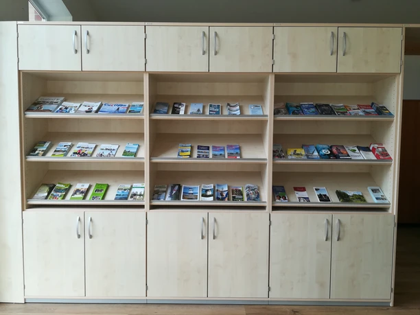 Een lichte houten displaywand vol kleurrijke folders die uitnodigen tot allerlei vakantie-avonturen.