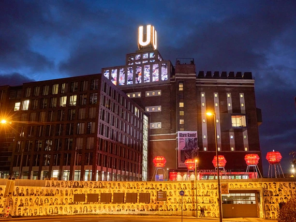Dortmunder U bei Nacht, beleuchtet, mit roten Leuchten und fotografischen Portraits im Vordergrund.