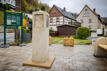 Caspar-David-Friedrich-Stele Steinsäule mit Relief auf gepflastertem Platz, umgeben von Fachwerkhäusern und Infotafel; herbstliche Stimmung.