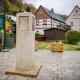 Caspar-David-Friedrich-Stele Steinsäule mit Relief auf gepflastertem Platz, umgeben von Fachwerkhäusern und Infotafel; herbstliche Stimmung.Stone column with relief on paved square, surrounded by half-timbered houses and information board; autumnal atmosphere.Kamenný sloup s reliéfem na dlážděném náměstí, obklopený hrázděnými domy a informační tabulí; podzimní atmosféra.Kamienna kolumna z płaskorzeźbą na brukowanym placu, otoczona domami z muru pruskiego i tablicą informacyjną; jesienna atmosfera.Stenen zuil met reliëf op geplaveid plein, omringd door vakwerkhuizen en informatiebord; herfstsfeer.Colonna in pietra con rilievo su piazza lastricata, circondata da case a graticcio e pannello informativo; atmosfera autunnale.