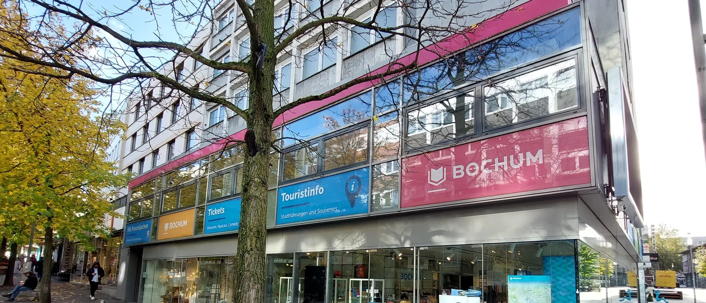 Bochum Touristinfo_Bochum Marketing GmbH, Astrid Jordan.jpg Blick auf die Glasfassade der Touristinfo mit einem Baum im Vordergrund sowie Werbebeklebung an den Scheiben