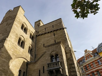 Eigelsteintorburg Die Eigelsteintorburg in Köln ist ein imposantes, historisches Bauwerk aus Sandstein. Auf dem Bild ist die massive Fassade mit ihren markanten Bögen und Türmen zu sehen, die in den blauen Himmel ragen. Rechts im Vordergrund steht ein Baum, dessen Blätter einen Kontrast zur Architektur bilden. Im Hintergrund sind bunte Hausfassaden zu erkennen, die einen urbanen Kontext hinzufügen.The Eigelsteintorburg in Cologne is an imposing, historic building made of sandstone. The picture shows the massive façade with its striking arches and towers rising into the blue sky. On the right in the foreground is a tree whose leaves form a contrast to the architecture. In the background, colorful house facades can be seen, adding an urban context.
