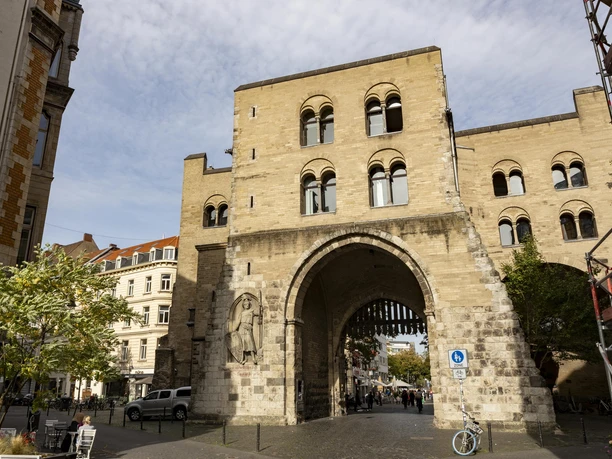 Eigelstein City Gate The picture shows the impressive Eigelstein City Gate in Cologne, a medieval gate castle in sandstone construction with three storeys, arches and historical details. It is surrounded by houses and shows a typical urban Cologne street scene.
