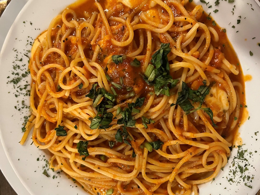 Spaghetti Ein Teller Spaghetti in Tomatensauce, garniert mit frischem Basilikum und Kräutern, wird von oben gezeigt.