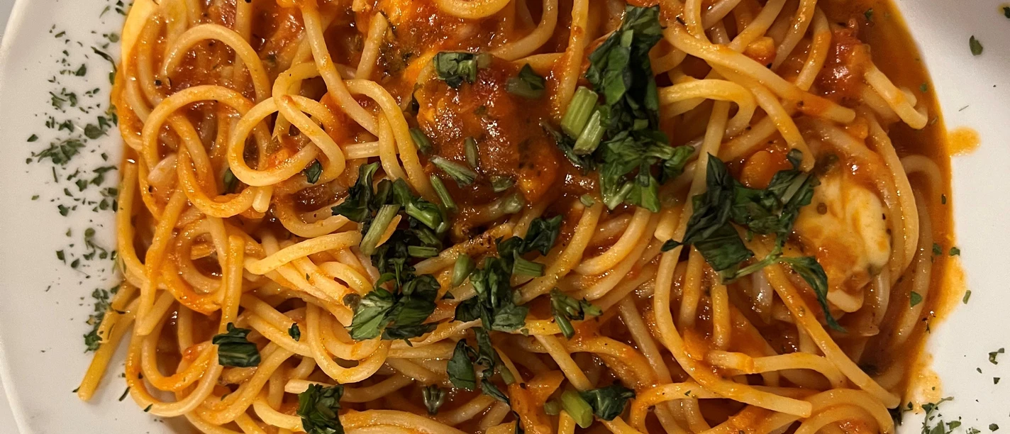 Spaghetti Ein Teller Spaghetti in Tomatensauce, garniert mit frischem Basilikum und Kräutern, wird von oben gezeigt.