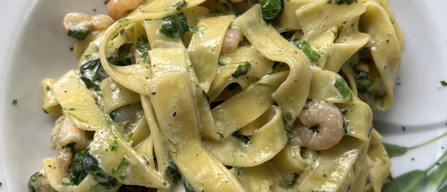 Lintnoedels met garnalen, verse kruiden en spinazieblaadjes geserveerd op een wit bord.