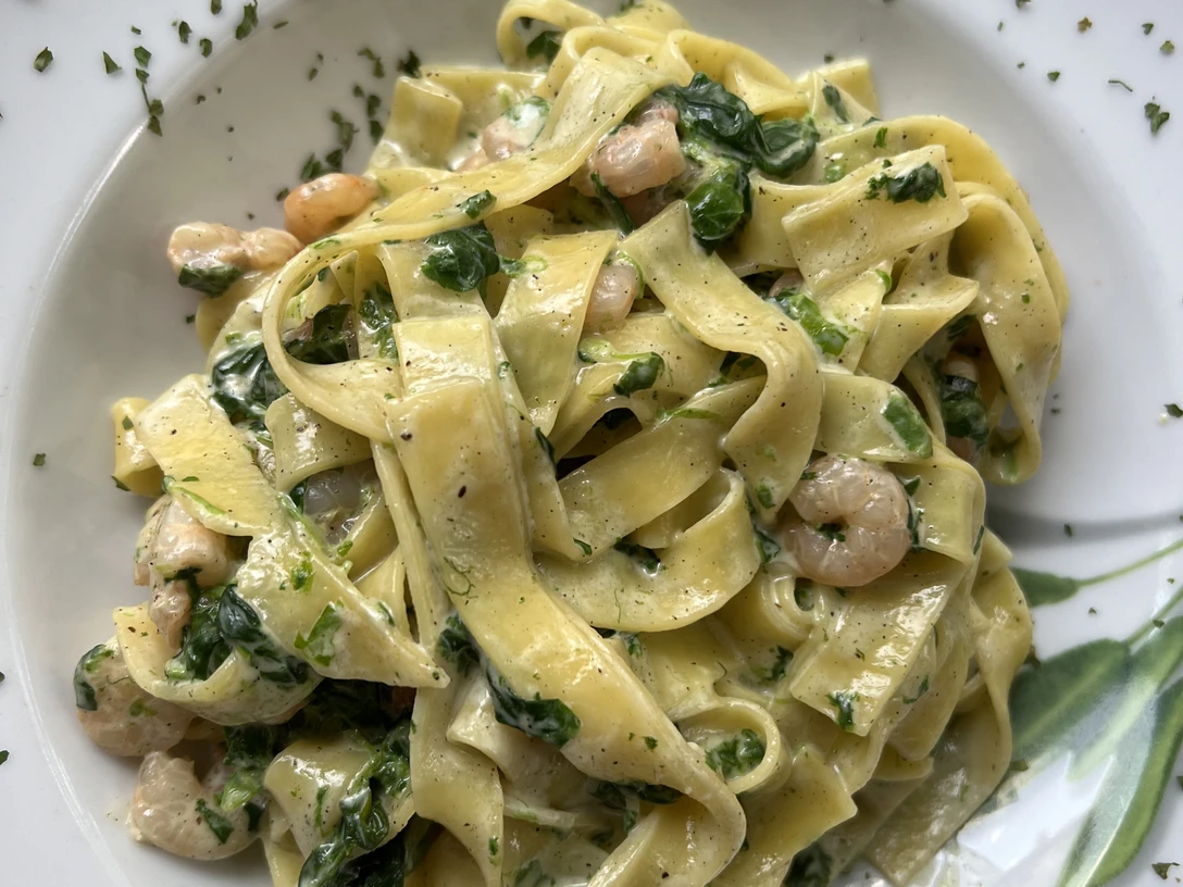 Nudeln mit Krabben Bandnudeln mit Garnelen, frischen Kräutern und Spinatblättern auf einem weißen Teller serviert.