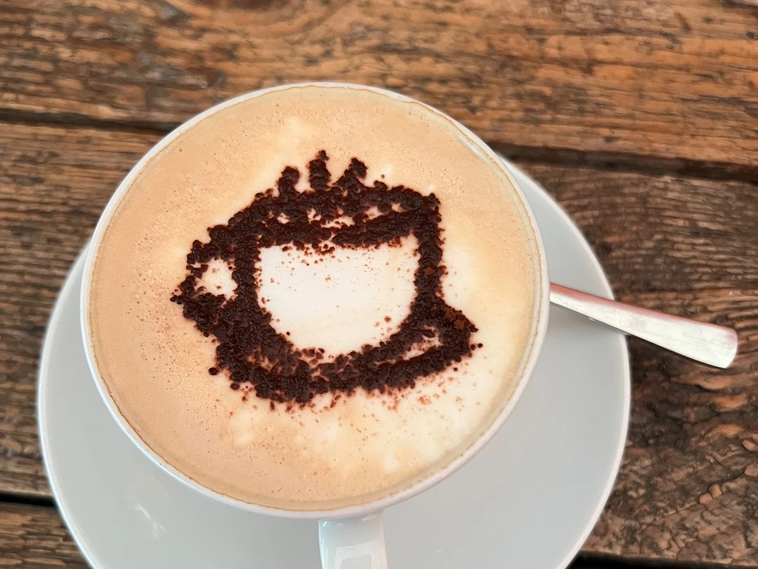 Eine Cappuccino-Tasse mit Kakaopulver-Motiv auf schaumiger Milch, serviert auf einem Holztisch.