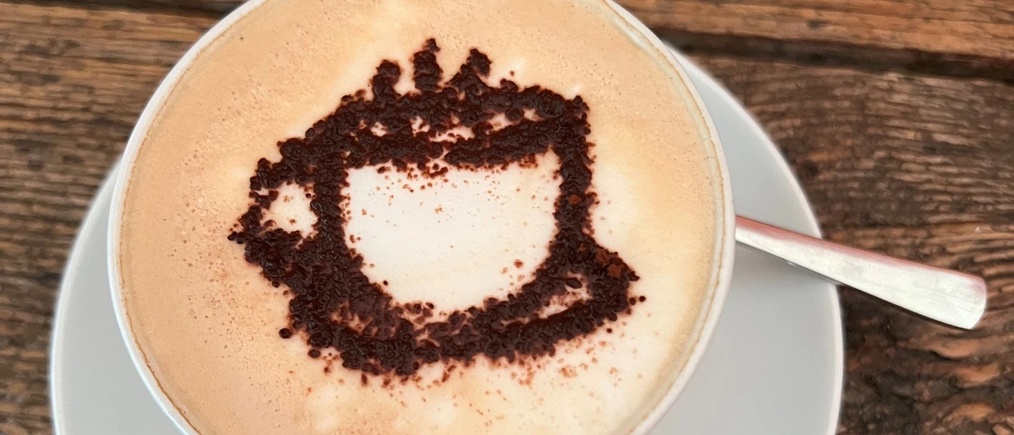 A cappuccino cup with a cocoa powder motif on frothy milk, served on a wooden table.