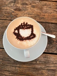 Cappucino Eine Cappuccino-Tasse mit Kakaopulver-Motiv auf schaumiger Milch, serviert auf einem Holztisch.