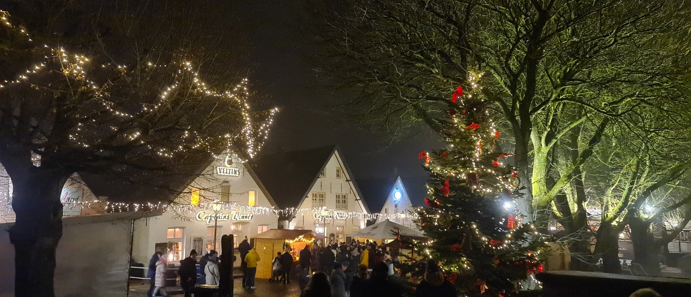 Weihnachtsmarkt Greetsiel Je kunt het uitzicht op de kerstmarkt zien in het donker met feeërieke lichtjes. Aan de voorkant staat een grote versierde kerstboom.