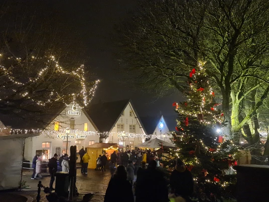 Weihnachtsmarkt Greetsiel Zu sehen ist der Blick auf den Weihnachtsmarkt bei Dunkelheit und mit Lichterketten. Vorne steht eine große geschmückte Weihnachtstanne. You can see the view of the Christmas market in the dark with fairy lights. In front is a large decorated Christmas tree.Du kan se udsigten til julemarkedet i mørket med lyskæder. Foran står et stort pyntet juletræ.Je kunt het uitzicht op de kerstmarkt zien in het donker met feeërieke lichtjes. Aan de voorkant staat een grote versierde kerstboom.
