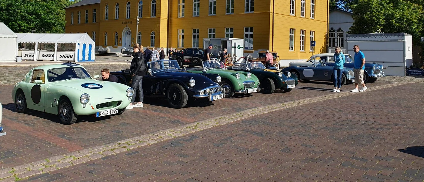 Rallye_Oldtimer.jpg Mehrere Oldtimer stehen vor dem Rathaus auf dem Parkplatz. Menschen schauen sie interessiert an