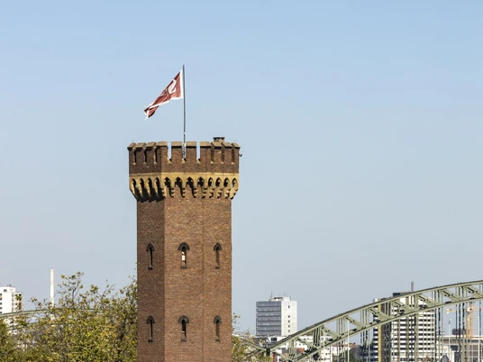 Malakoff Tower Der Malakoffturm in Köln ragt majestätisch vor der Kulisse des Flusses auf. Der markante Backsteinturm mit seinen Zinnen und der Flagge vereint historische Architektur und moderne Rheinansicht harmonisch.The Malakoff Tower in Cologne rises majestically against the backdrop of the river. The striking brick tower with its battlements and flag harmoniously combines historical architecture and a modern view of the Rhine.